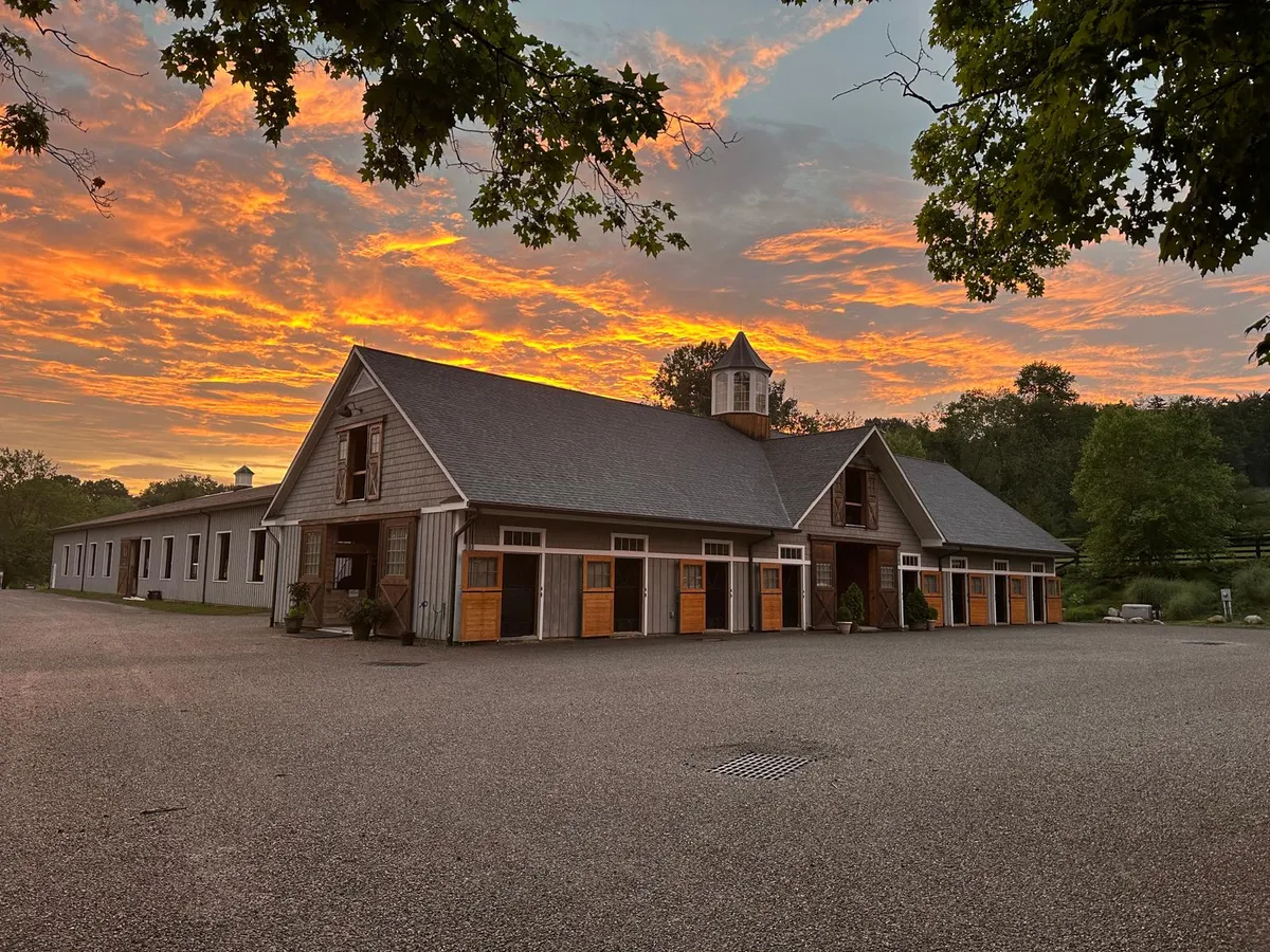 The grey wooden stable block at sunset, with a cupola on the roof