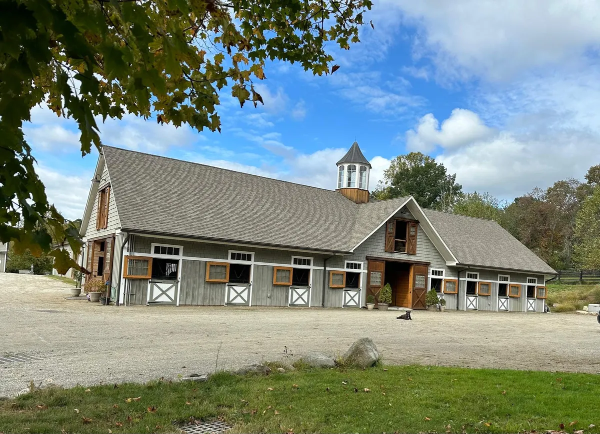 The grey wooden stable block with stable doors and windows under a blue sky