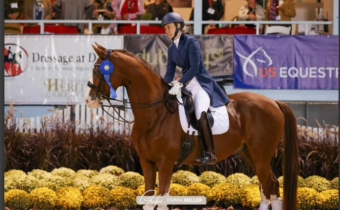 Mica Mabragaña with a chestnut horse and a blue rosette in front of the Dressage at Devon banners